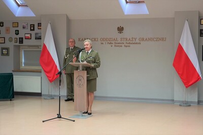 Pani Komendant karpackiego oddziału straży granicznej przemawia do zebranych podczas uroczystości. w tle widoczne flagi Polski w kolorze białoczerwonym. za panią komendant obecny jest zastępca komendanta oddziału.