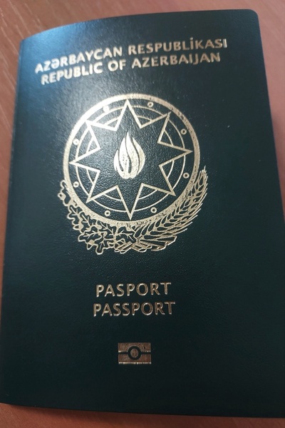 na zdjęciu widoczny paszport Azerbejdżanu koloru czarnego ze złotymi napisami. położony jest on na blacie biurka.