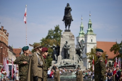 Plac jana matejki w krakowie. Przed pomnikiem stoją w warcie honorowej żołnierze. powiewają biało czerwone flagi, w tle uczestnicy uroczystości