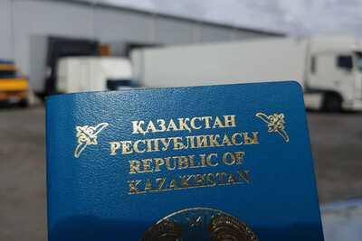 paszport Kazachstanu w kolorze niebieskim ze złotymi napisami. w tle znajdują się pojazdy ciężarowe oraz budynki firmowe.