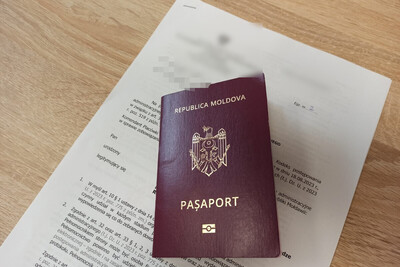 paszport Mołdawii w kolorze bordowym ze złotymi napisami położony na papierowej decyzji o zobowiązaniu do powrotu. całość ułożona na biurku.