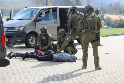 na tle ołtarza papieskiego w starym sączu, funkcjonariusze SG z WZD dokonują dynamicznego zatrzymania pozorantów- terrorystów. stoją dwa samochody. jedne z zatrzymany leży twarzą do ziemi. Funkcjonariusze zabezpieczają teren