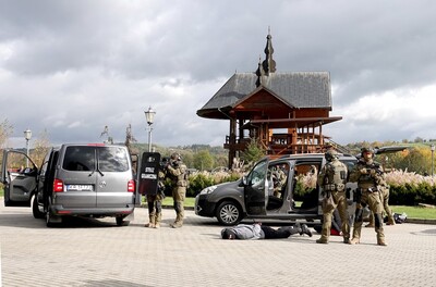 na tle ołtarza papieskiego w starym sączu, funkcjonariusze SG z WZD dokonują dynamicznego zatrzymania pozorantów- terrorystów. stoją dwa samochody. jedne z zatrzymany leży twarzą do ziemi. Funkcjonariusze zabezpieczają teren