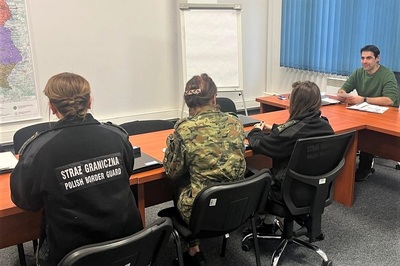 funkcjonariusze kaosg siedzą przy stole podczas lekcji z native-spikerem, w tle tablica.