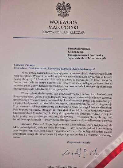 zdjęcie listu skierowanego do obchodzących święto niepodległości służb mundurowych komendantów, funkcjonariuszy i pracowników sądeckich służb mundurowych. list przepasany jest w prawym dolnym rogu biało-czerwoną wstążką