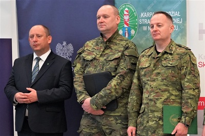 przedstawiciele straży granicznej wraz z wojewodą małopolskim stoją na tle rolapów służb.