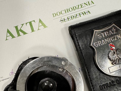 Na teczce z napisem akta dochodzenia leży metalowa odznaka funkcjonariusza sg oraz kajdanki