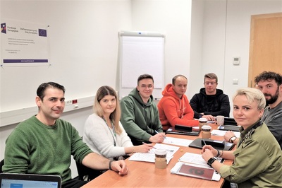 Funkcjonariusze sg siedzą przy stole, na którym leża notatki i materiały do nauki języka angielskiego. wśród nich siedzi lektor.