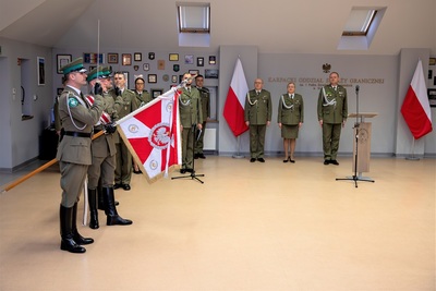 sala odpraw. poczet sztandarowy pochyla sztandar kaosg. w tle stoją uczestnicy uroczystości