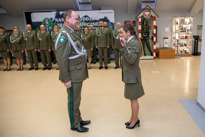 sala odpraw.  odchodząca na emeryturę funkcjonariuszka całuje szablę oficerską. w tle uczestnicy uroczystości