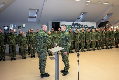 na pierwszym planie widoczny dowódca uroczystości który składa meldunek komendantowi oddziału.  w tle stoją  funkcjonariusze straży granicznej. całość odbywa się w sali odpraw oddziału.