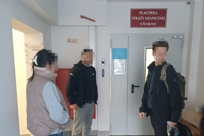 Kobieta i dwóch mężczyzn zatrzymani cudzoziemcy stoją przed wejściem do pomieszczeń Placówki SG w Krakowie