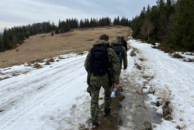 funkcjonariusze straży granicznej idą szlakiem górskim wzdłuż granicy Polsko słowackiej. widoczny śnieg oraz lasy.