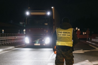 noc widać nadjeżdżającego tira, przed nim w odblaskowej kamizelce stoi funkcjonariusz sg, na jego plecach napis straż graniczna polish border guard