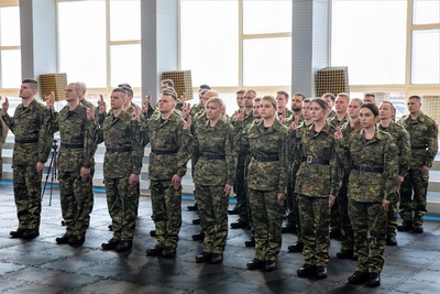 Nowo przyjęci funkcjonariusze z podniesionymi do ślubowania dłońmi z wysuniętymi dwoma palcami stoją w szyku. jest ich 29 osób