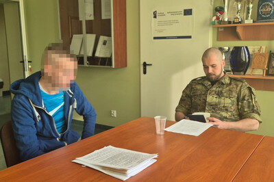 Przy stole siedzi zatrzymany Ukrainiec i funkcjonariusz sg. Strażnik graniczny przegląda paszport