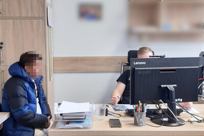 Zatrzymany cudzoziemiec siedzi przy biurku. Za monitorem komputera siedzi funkcjonariusz sg