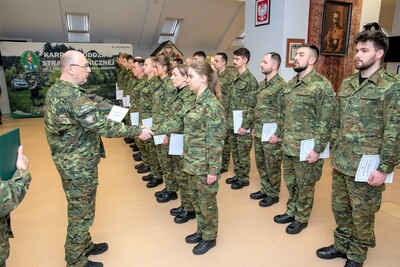 kilkunastu  funkcjonariuszy mianowanych na stopień kaprala stoi na baczność. płk marcisz wręcza jednemu z nich akt mianowania na stopień