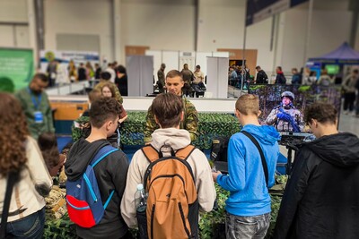 Targi kraków expo. funkcjonariusz stoi przy stoisku promocyjnym kaosg. Przed nim zainteresowani uczestnicy targów zadający pytania i zapoznający się ze sprzętem na codzień używanym przez funkcjonariuszy sg