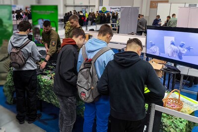 Targi kraków expo. funkcjonariusz stoi przy stoisku promocyjnym kaosg. Przed nim zainteresowani uczestnicy targów zadający pytania i zapoznający się ze sprzętem na codzień używanym przez funkcjonariuszy sg