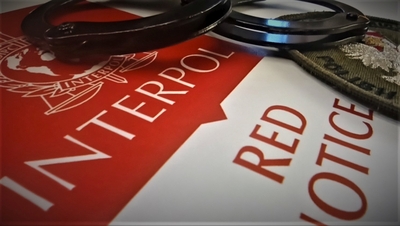 Kajdanki koloru czarnego wraz z emblematem straży granicznej do umundurowania polowego na tle czerwono białym z napisami Interpol red notice, oraz logiem Interpolu