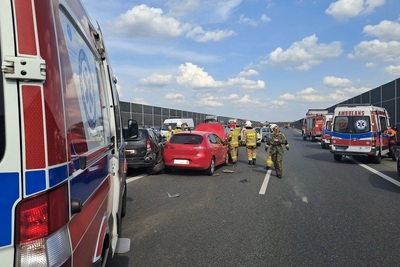 na zdjęciu widoczne jest zdarzenie drogowe. wypadek ma miejsce na autostradzie. na pierwszym planie widoczne sa karetki pogotowia . w tle widoczne są samochody biorące udział w kolizji i helikopter ratownictwa medycznego.