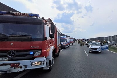 na zdjęciu widoczne jest zdarzenie drogowe. wypadek ma miejsce na autostradzie. na pierwszym planie widoczny pojazd służbowy straży pożarnej oraz pojazdy karetek pogotowia. w tle widoczne są samochody biorące udział w kolizji.