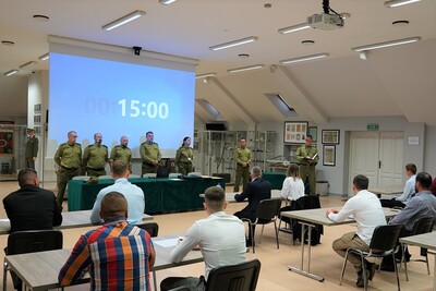 na pierwszym planie widoczni są kandydaci aplikujący do służby w straży granicznej. na drugim planie widoczna jest komisja egzaminacyjna  złożona z funkcjonariuszy straży granicznej. do kandydatów mówi przewodniczący komisji egzaminacyjnej. całość odbywa się w sali odpraw karpackiego oddziału straży granicznej. na telebimie widoczny jest czas do zakończenia testu.