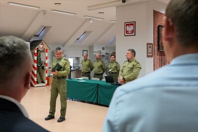 na pierwszym planie widoczna jest komisja egzaminacyjna  złożona z funkcjonariuszy straży granicznej. do kandydatów mówi przewodniczący komisji egzaminacyjnej. widoczni są kandydaci aplikujący do służby w straży granicznej. na drugim planie widoczna . całość odbywa się w sali odpraw karpackiego oddziału straży granicznej.