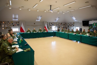 Funkcjonariusze ubrani w mundur polowy siedzą wokół stołu ułożonego w literę U, w głównym miejscu siedzą Komendanci Karpackiego oddziału straży granicznej