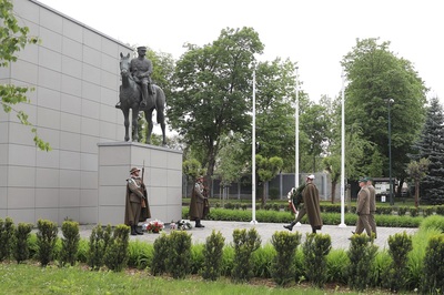 na zdjęciu widoczni są funkcjonariusze straży granicznej którzy składają wieniec przed pomnikiem marszałka Piłsudskiego.  przed pomnikiem stoją funkcjonariusze tworzący posterunek honorowy. stoją na baczność przed pomnikiem marszałka Piłsudskiego.  ubrani są w mundur galowy wraz z peleryną oraz kapeluszem. w dłoniach trzymają karabin reprezentacyjny. pomnik marszałka Piłsudskiego przedstawia marszałka który siedzi na koniu. w tle widać wielki mur który tworzy tło dla pomnika.