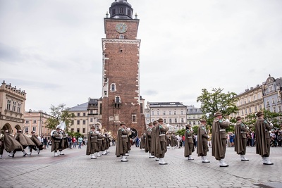 Orkiestra reprezentacyjna straży granicznej grająca na rynku w Krakowie w tle wieża sukiennic w koło ludzie oglądający musztrę paradna straży granicznej