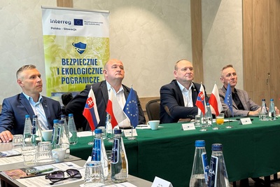4 mężczyzny siedzących za stołem ubranych w marynarki słuchający wykładu