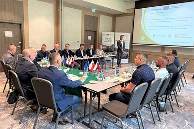 Mężczyźni ubrani w marynarki siedzący za stołami słuchający wykładu na ekranie projektora wyświetlana prezentacja