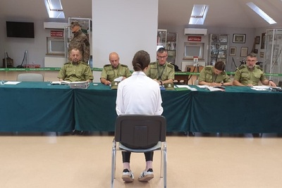 Kandydatka na funkcjonariusz straży granicznej podczas rozmowy kwalifikacyjnej siedząca na przeciw komisji rekrutacyjnej składającej się z funkcjonariuszy straży granicznej ubrani są w mundur służbowy koloru zielonego