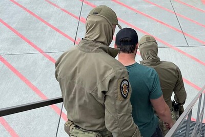 Zamaskowani dwaj funkcjonariusze krakowskiego Zespołu Interwencji Specjalnych sprowadzają po schodach samolotu deportowanego Polaka
