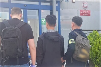 Zatrzymany obywatel chin jest wprowadzany po schodach przez dwóch nieumundurowanych funkcjonariuszy straży granicznej do siedziby placówki sg w krakowie