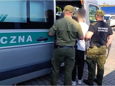 Na zdjęciu funkcjonariusze zatrzymują mężczyznę i prowadzą go do służbowego pojazdu. Na koszulce funkcjonariuszy napis Straż Graniczna.