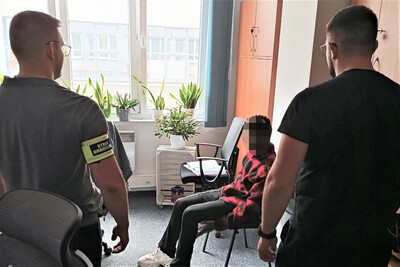 Zatrzymany nigeryjczyk siedzi na krześle w pomieszczeniach biurowych placówki Sg w  krakowie. Pilnuje go dwóch nieumundurowanych funkcjonariuszy sg