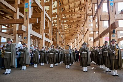 Orkiestra SG w paradnych mundurach z bębnami i instrumentami dętymi, grająca w drewnianej hali.