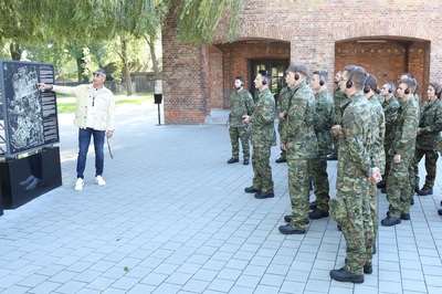 Funkcjonariusze sg słuchają przewodnika muzeum auschwitz-birkenau, który wskazuje na tablicach miejsca o których opowiada