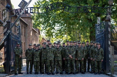 grupa funkcjonariuszy sg stoi pod historyczną bramą wejściową do obozu w oświęcimiu, na której widnieje napis arbeit macht frei