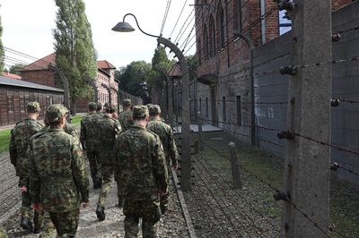 funkcjonariusze sg idą wśród drutów kolczastych po żwirowej drodze wśród bloków w których kiedyś przebywali uwiezieni w Auschwitz-Birkenau