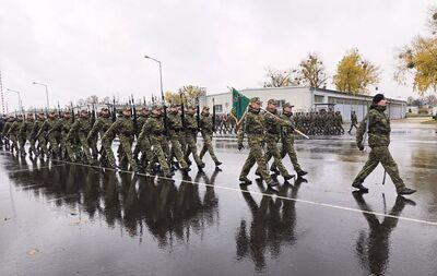 Na zdjęciu maszerują funkcjonariusze służby mundurowej prawdopodobnie Straży Granicznej. Kolumnę prowadzi dowódca uroczystości trzymając w ręce szablę. Tuż za nim trzech mężczyzn w mundurach, mężczyzna w środku trzyma w rękach sztandar. Za nimi kolumna mężczyzn w mundurach trzymają w rękach karabinki.