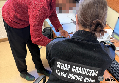 Zatrzymany cudzoziemiec podpisuje leżące na biurku dokumenty w asyście funkcjonariuszki straży granicznej