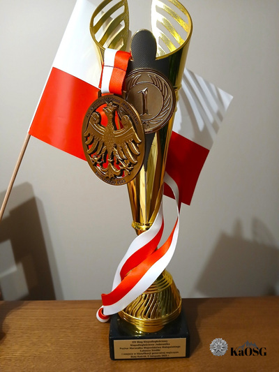 Na zdjęciu widać puchar za zajęcie 1 miejsca w biegu. Za nim widać małą flagę biało-czerwoną.