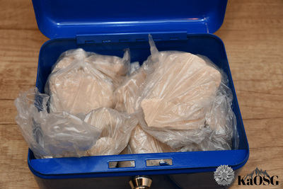Zbliżenie na niebieską skrzynkę, w której znajdują się worki foliowe z żółtawą zbryloną substancją