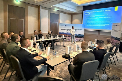 uczestnicy spotkania - kilkanaście osób - siedzą przy stole ułożonym w kształcie litery u. słuchają prelegenta.