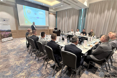 uczestnicy spotkania - kilkanaście osób - siedzą przy stole ułożonym w kształcie litery u. słuchają prelegenta.