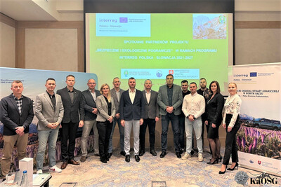 uczestnicy spotkania - kilkanaście osób - ustawili się do pamiątkowego zdjęcia . w tle ekran z prezentacją a po bokach banery z programu interreg i projektu